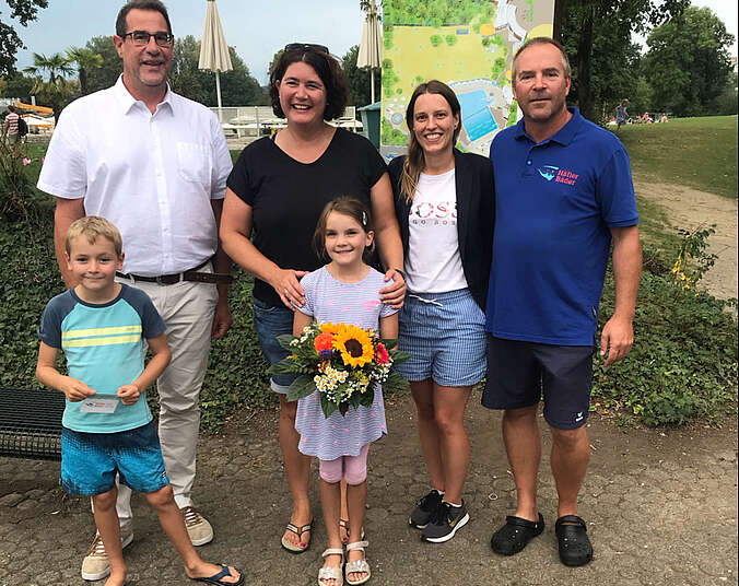 Eine Gruppe von Menschen stehen zusammen, die Frau hält einen Blumenstrauß in der Hand