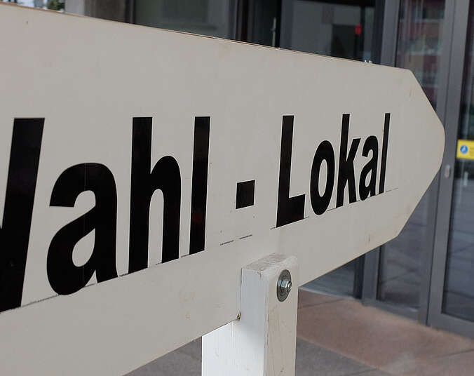 Schild mit Aufschrift "Wahl-Lokal" zeigt in Richtung gläserner Rathaus-Eingangstüre