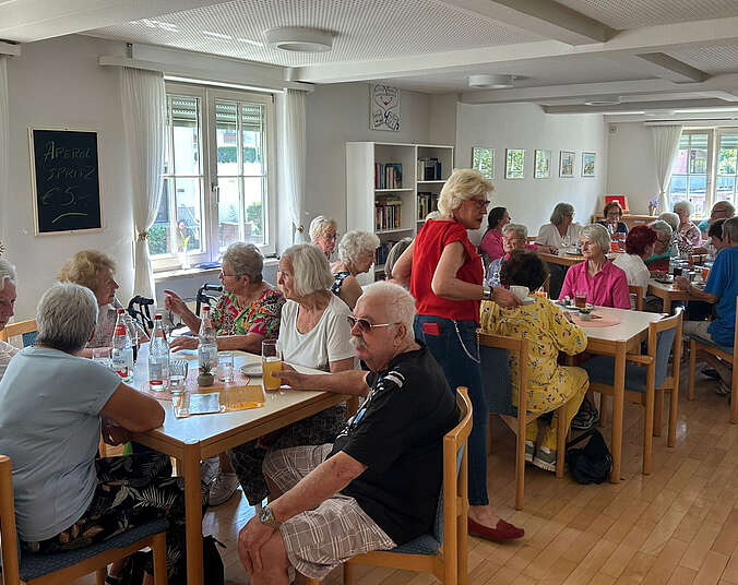 Frauen und Männer sitzen an Tischen und unterhalten sich