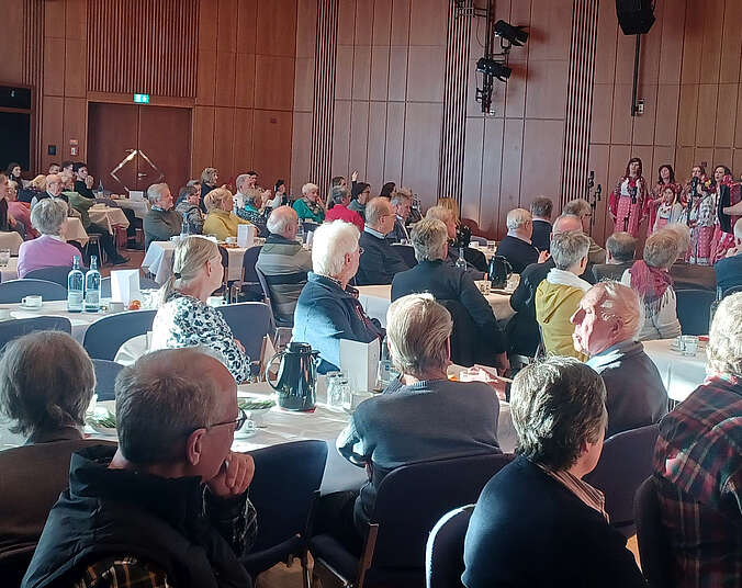 Männer und Frauen an Tischen bei Kaffee und Kuchen